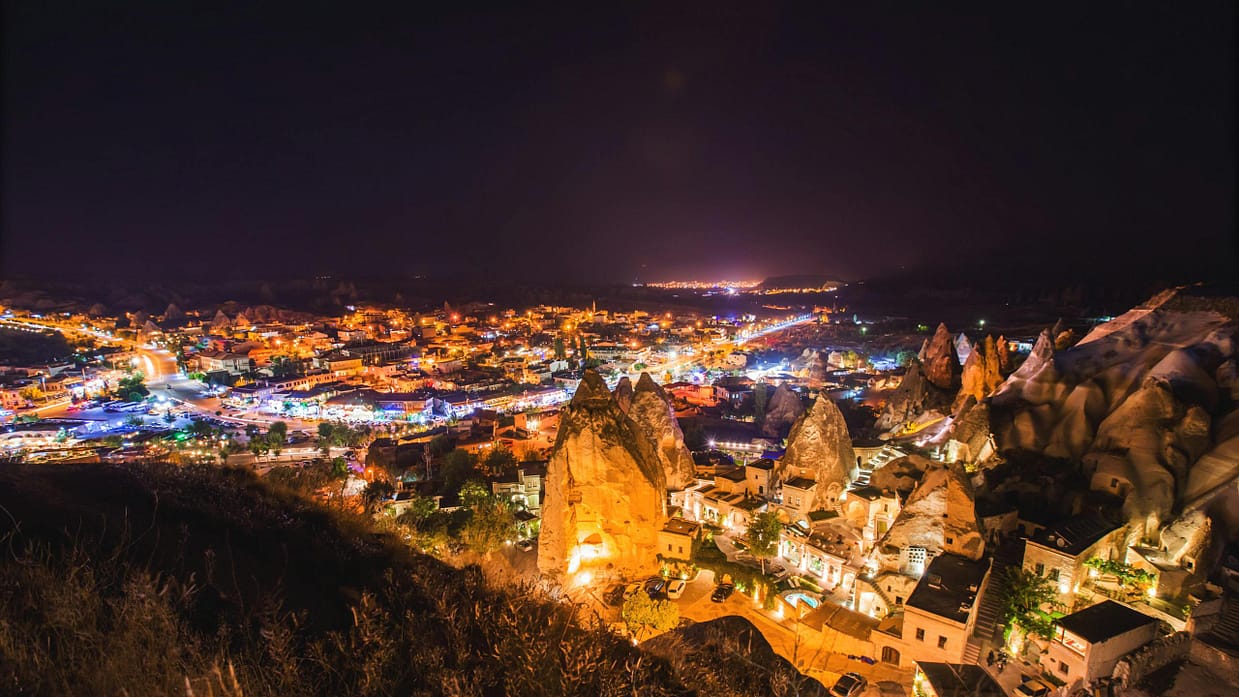 A vibrant nighttime aerial view of Göreme National Park with illuminated landmarks in Cappadocia, Turkey.