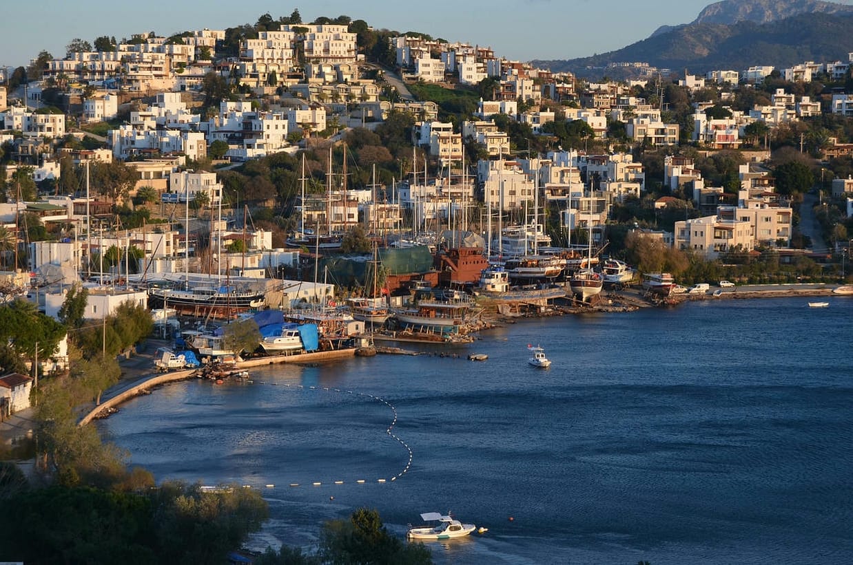 Beautiful panoramic view of Bodrum harbor with ships and waterfront houses at sunset.