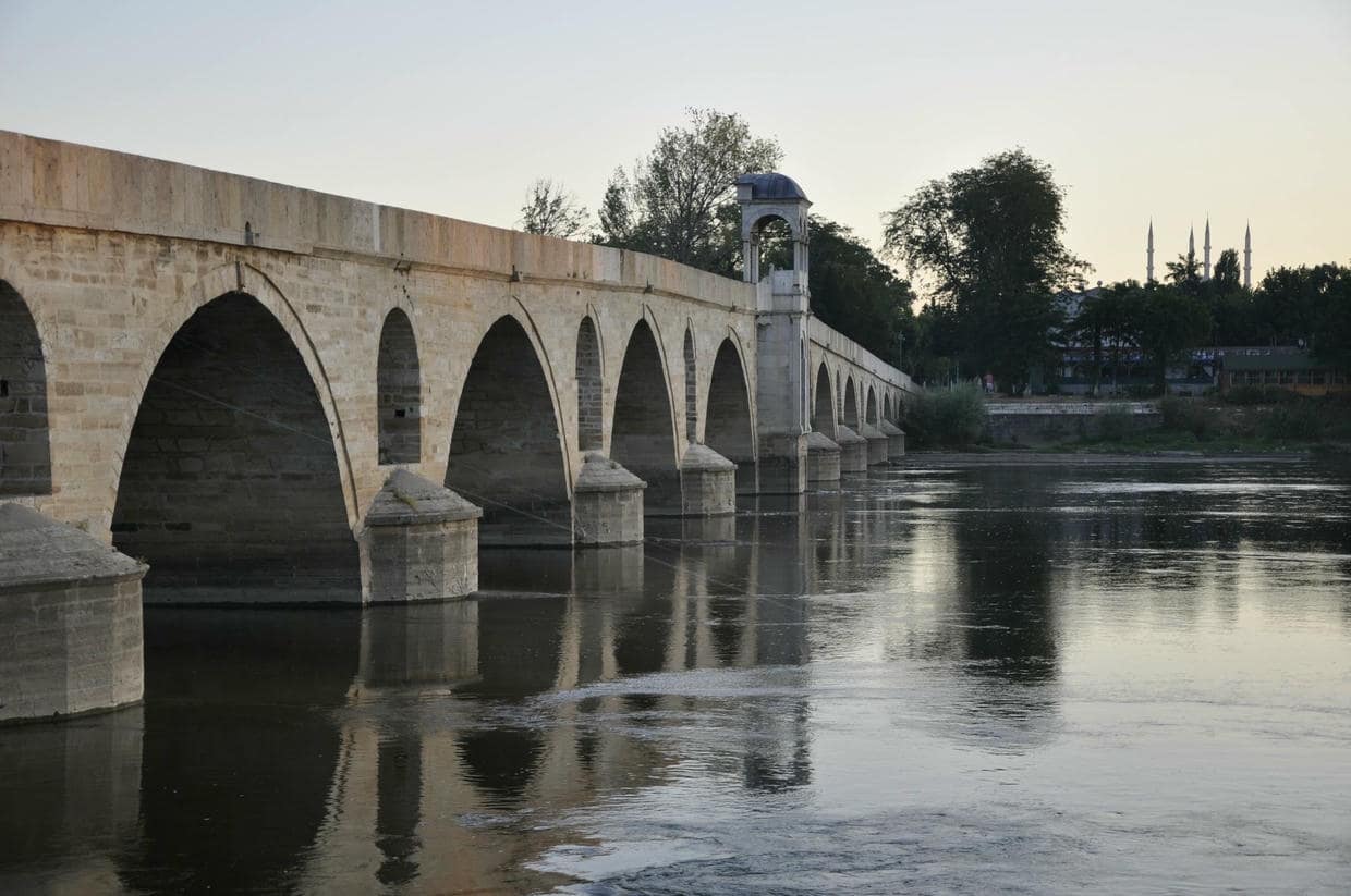 Iconic stone bridge over the Meriç River reflecting in tranquil waters at sunset in Edirne, Turkey.