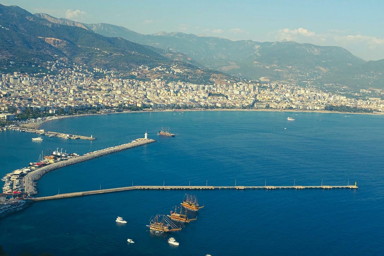 Discover the stunning aerial view of Alanya's vibrant harbor and coastline surrounded by mountains.