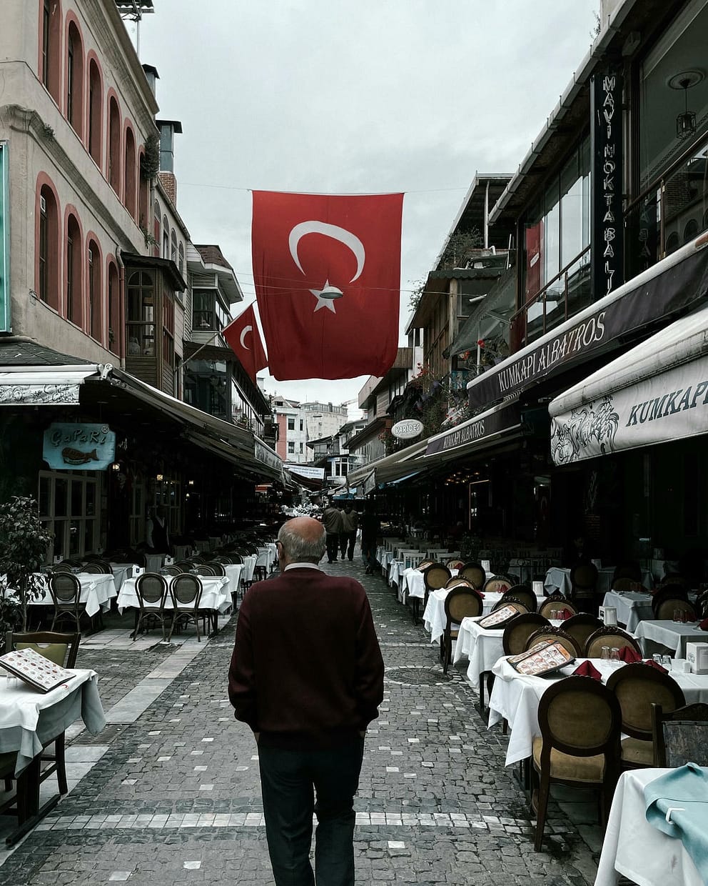 A man walks through a bustling street in Istanbul, lined with outdoor cafes and Turkish flags. Things to do in Turkey